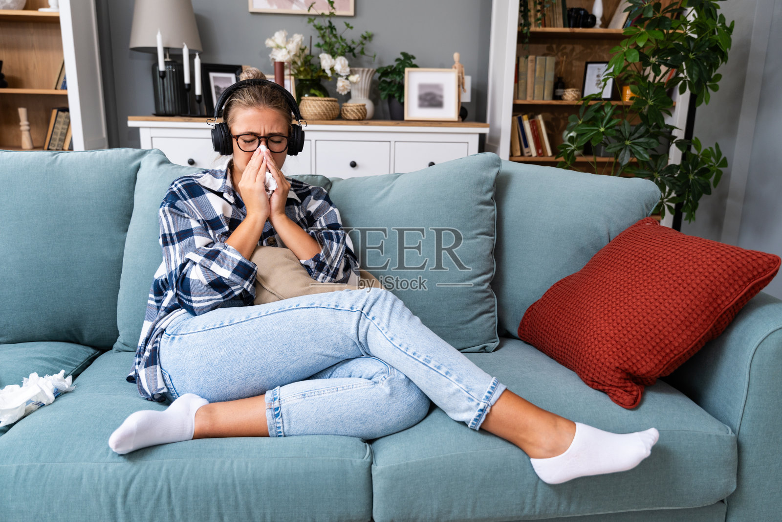 年轻悲伤的女孩独自坐在家里的沙发上，用无线耳机听着悲伤的音乐，一边哭一边用纸巾擦鼻子。记忆和缺失的概念。照片摄影图片