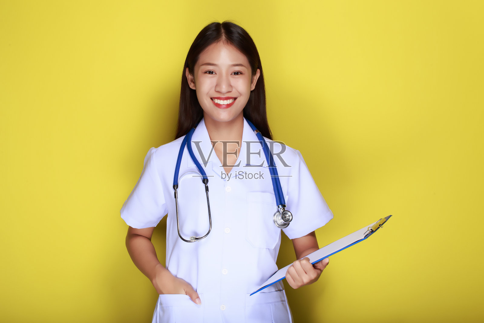 在黄色背景下，一位美丽的年轻女子的肖像，一位穿着医生制服的亚洲妇女露出微笑的表情，一位戴着医用听诊器的年轻女子露出友好的表情。照片摄影图片