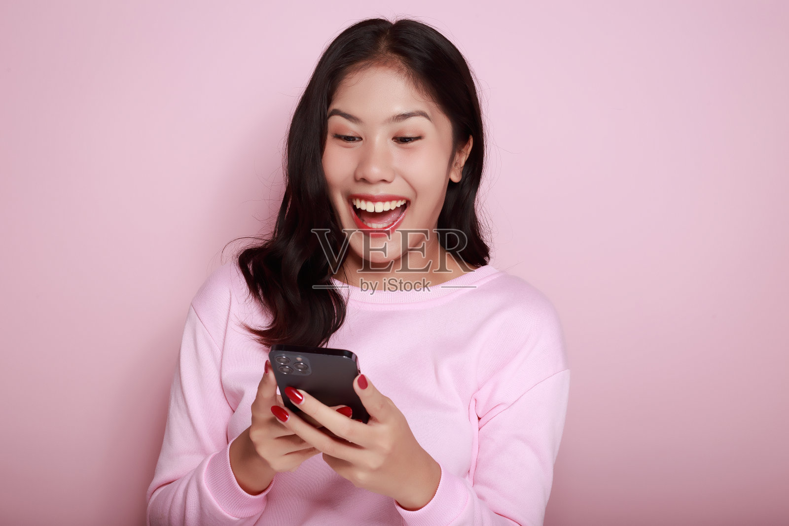 在浅粉色的背景下独自摆姿势。一个亚洲女人在电话里为某件事激动不已。漂亮积极的女士的半身照。照片摄影图片