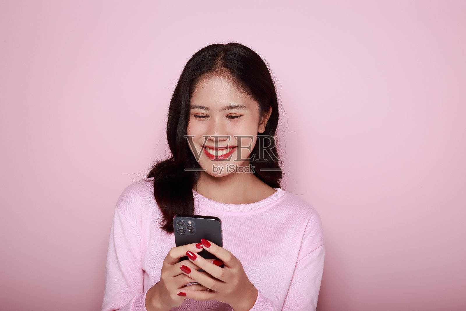 亚洲女子愉快地摆姿势与手机，一个美丽的年轻女子感到愉快和幸福。一个美丽的年轻女子的肖像在浅粉色的背景，照片摄影图片