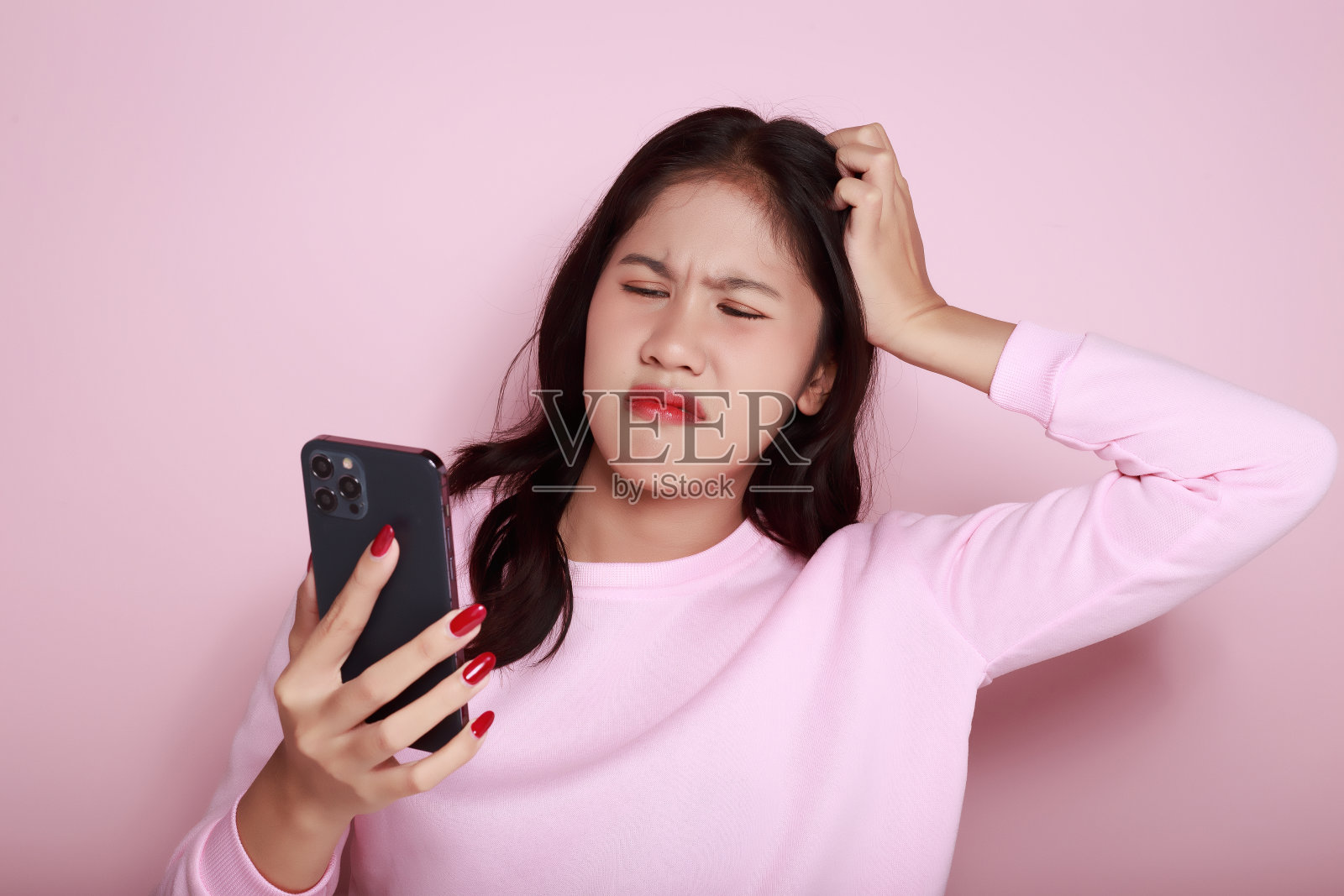 年轻女子用手机严肃的表情，一个美丽的年轻女子的肖像在浅粉色的背景，亚洲妇女摆姿势使用手机。照片摄影图片