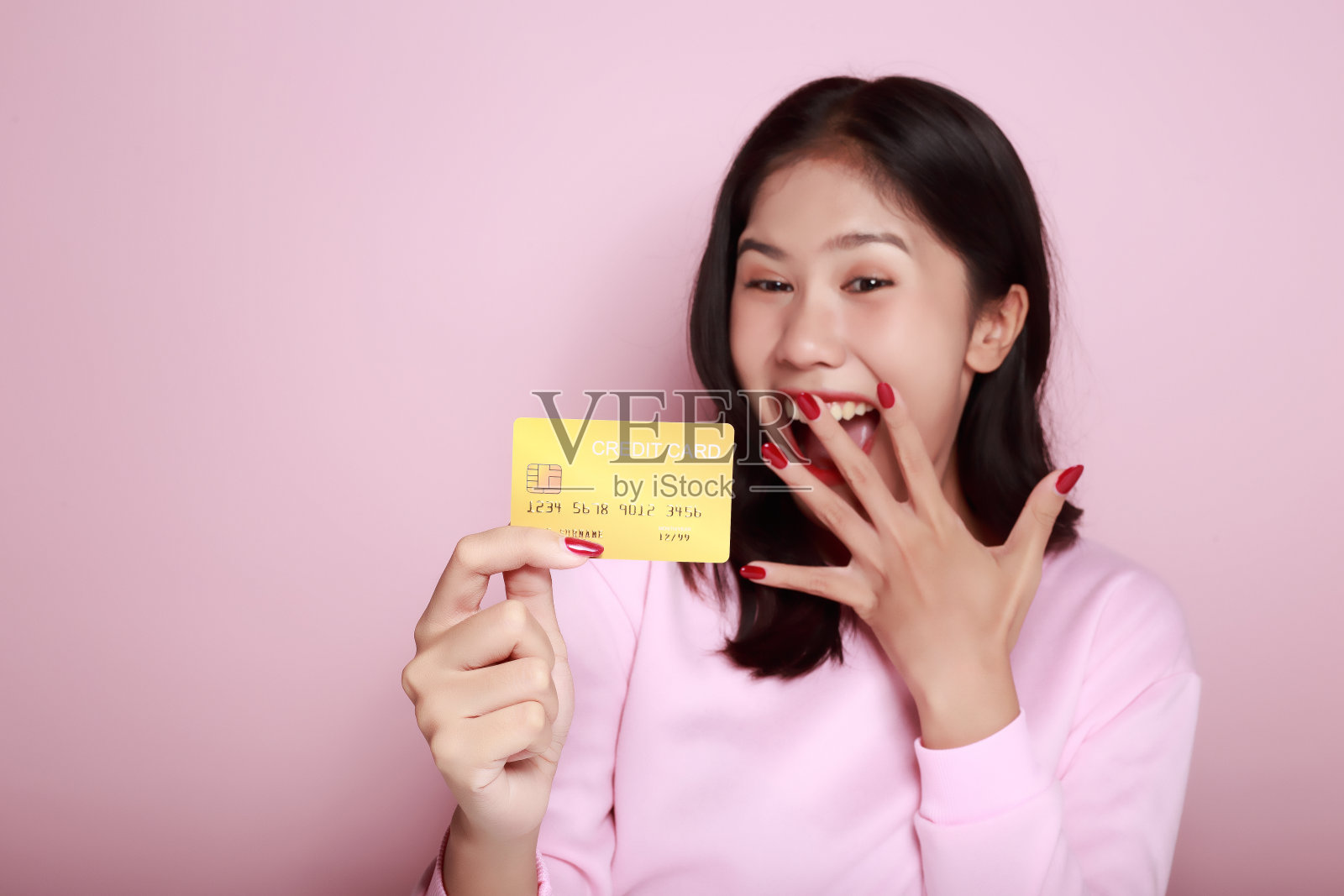 亚洲妇女手里拿着信用卡手里拿着借记卡一位美丽的年轻女子感到非常高兴和兴奋。浅粉色背景的肖像照片摄影图片