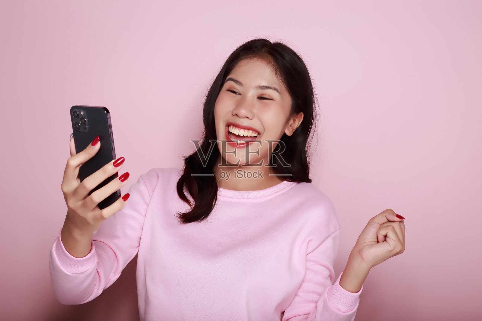 在浅粉色的背景下独自摆姿势。一个亚洲女人在电话里为某件事激动不已。漂亮积极的女士的半身照。照片摄影图片