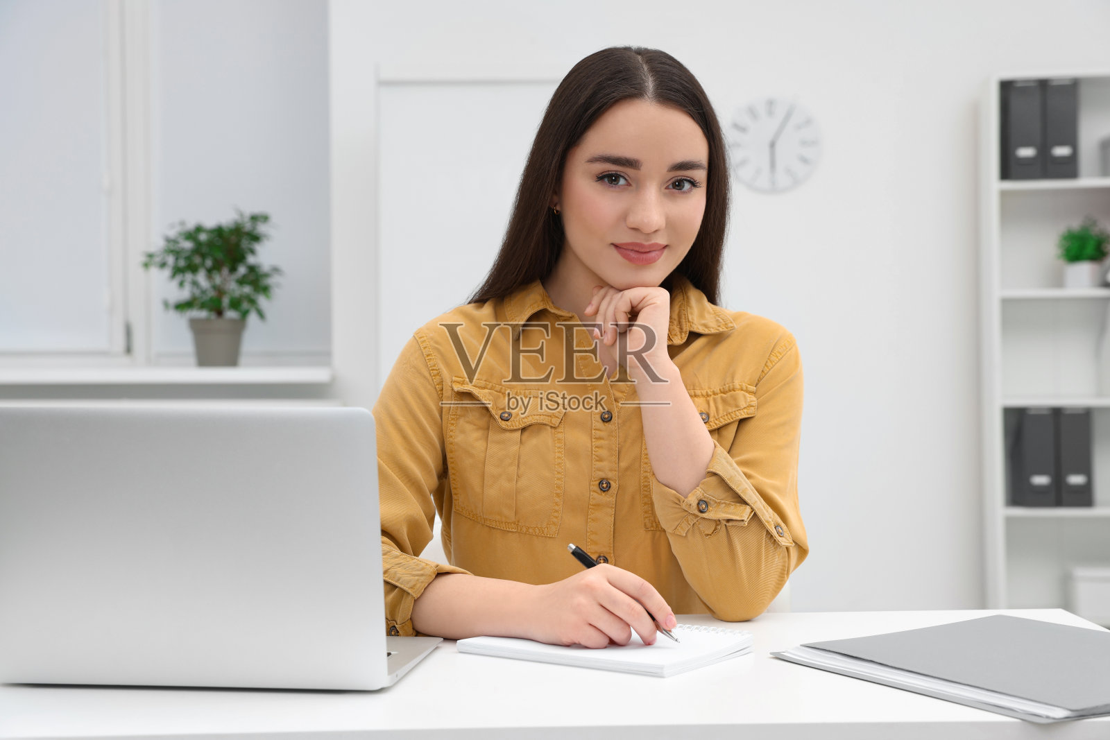 年轻的女实习生在办公室的桌子上用笔记本电脑工作照片摄影图片