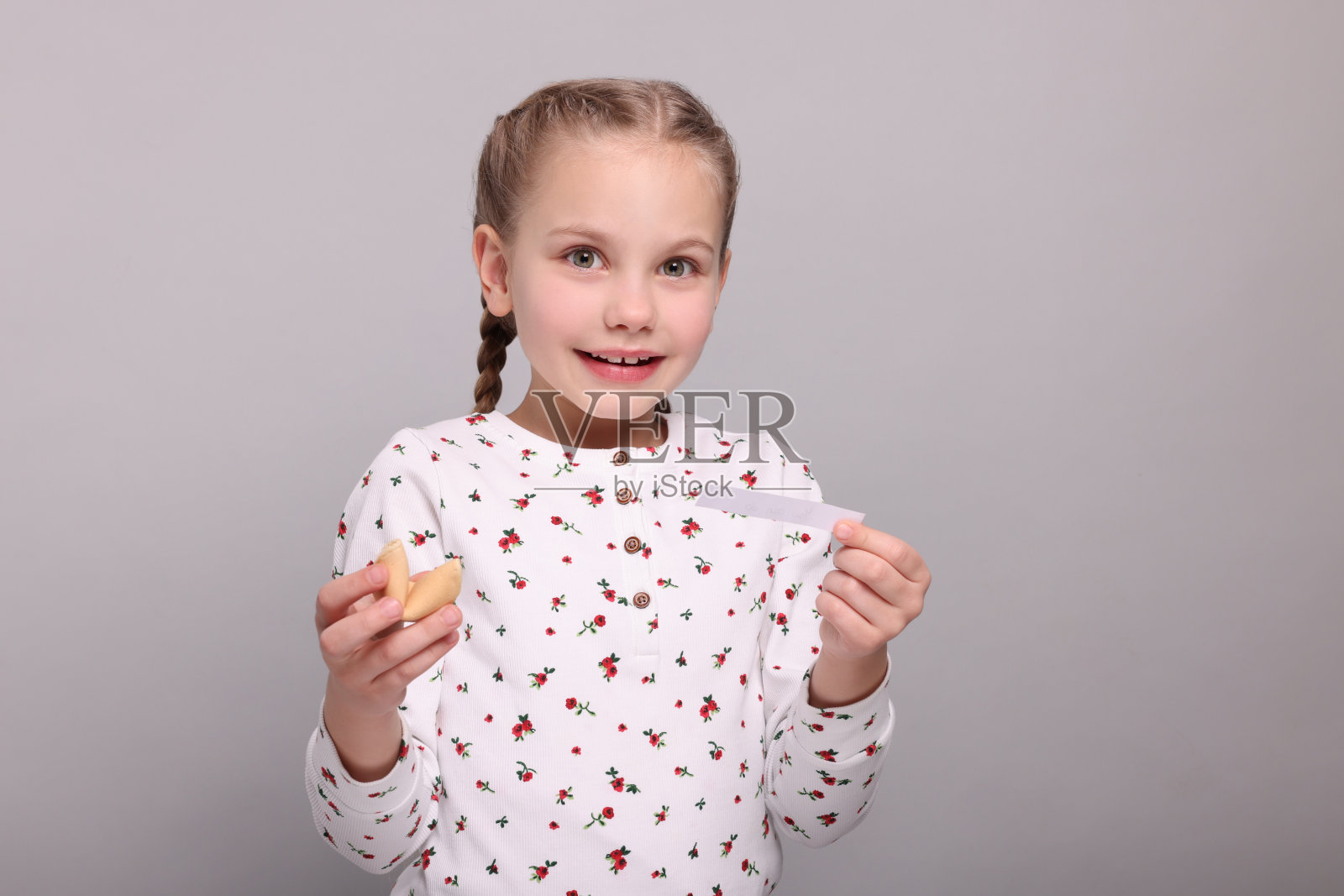 可爱的女孩拿着美味的幸运饼干，在浅灰色的背景上阅读预测照片摄影图片