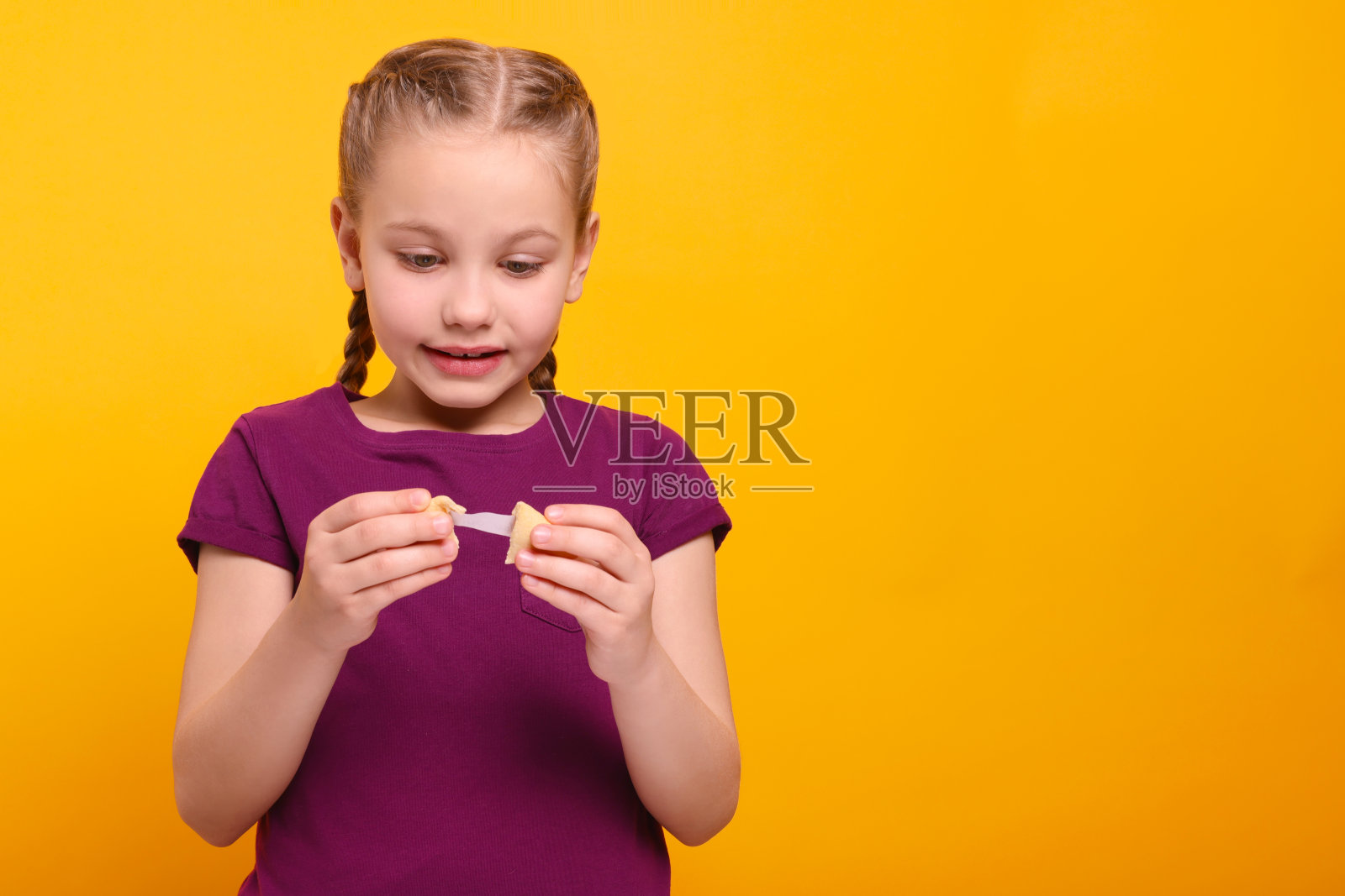 可爱的女孩拿着美味的幸运饼干，在橙色背景上阅读预测。文本空间照片摄影图片