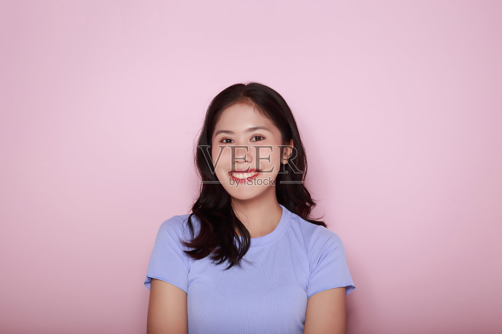 一个友好的微笑着的年轻女子的肖像，一个美丽的年轻女子的肖像在浅粉色的背景，快乐和微笑，张贴在站立的位置。照片摄影图片