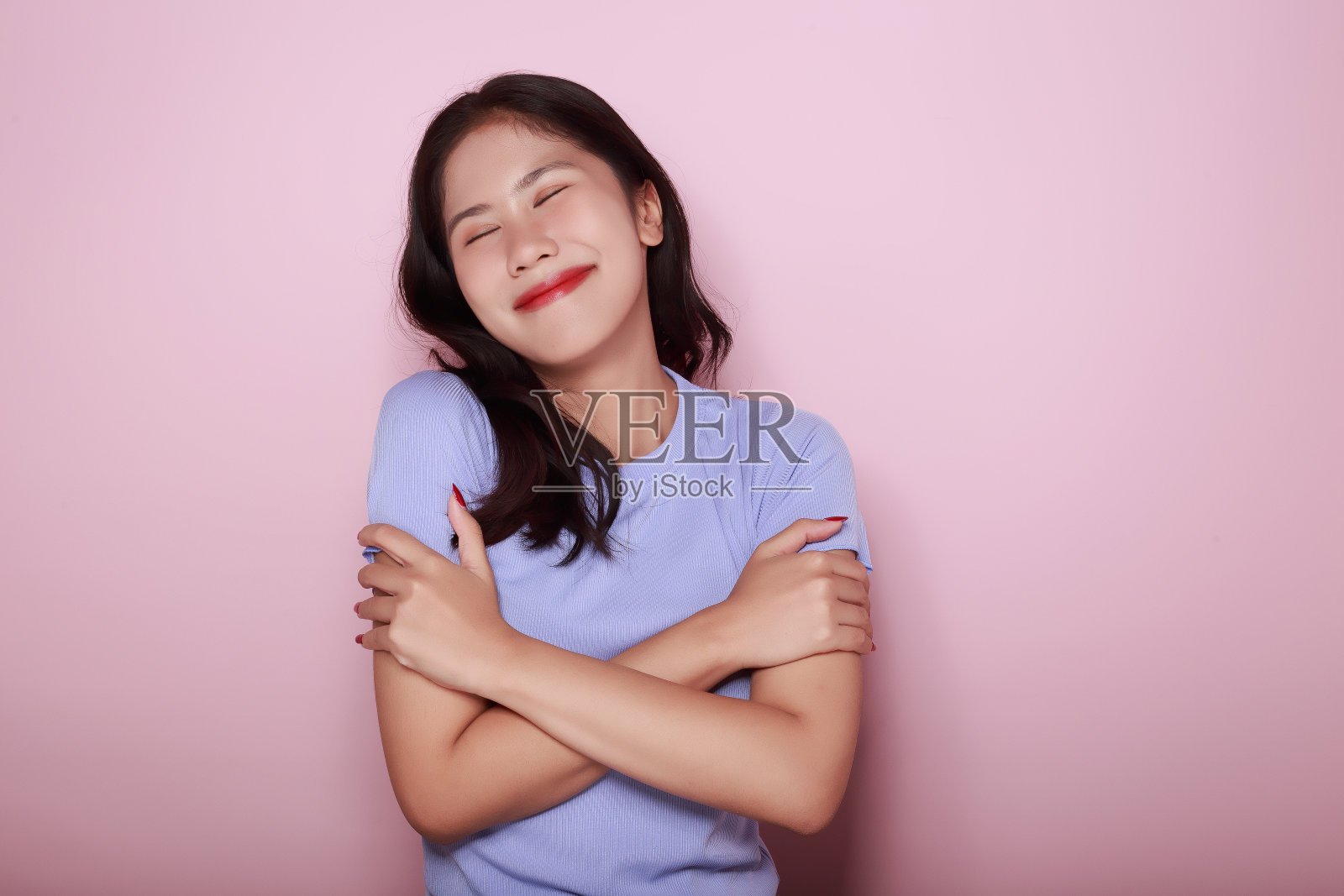 一个美丽的年轻女子的肖像，在浅粉色的背景下，快乐和微笑，张贴在站立的位置，半身照片的好积极的女士交叉臂摆空和孤立。照片摄影图片