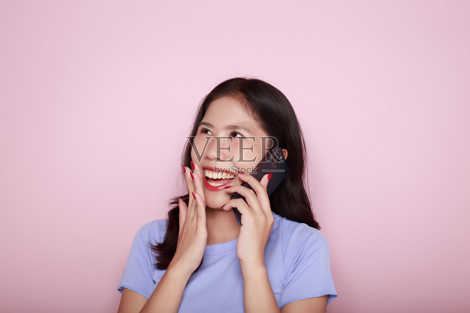 亚洲女子愉快地摆姿势与手机，一个美丽的年轻女子感到愉快和幸福。一个美丽的年轻女子的肖像在浅粉色的背景，照片摄影图片