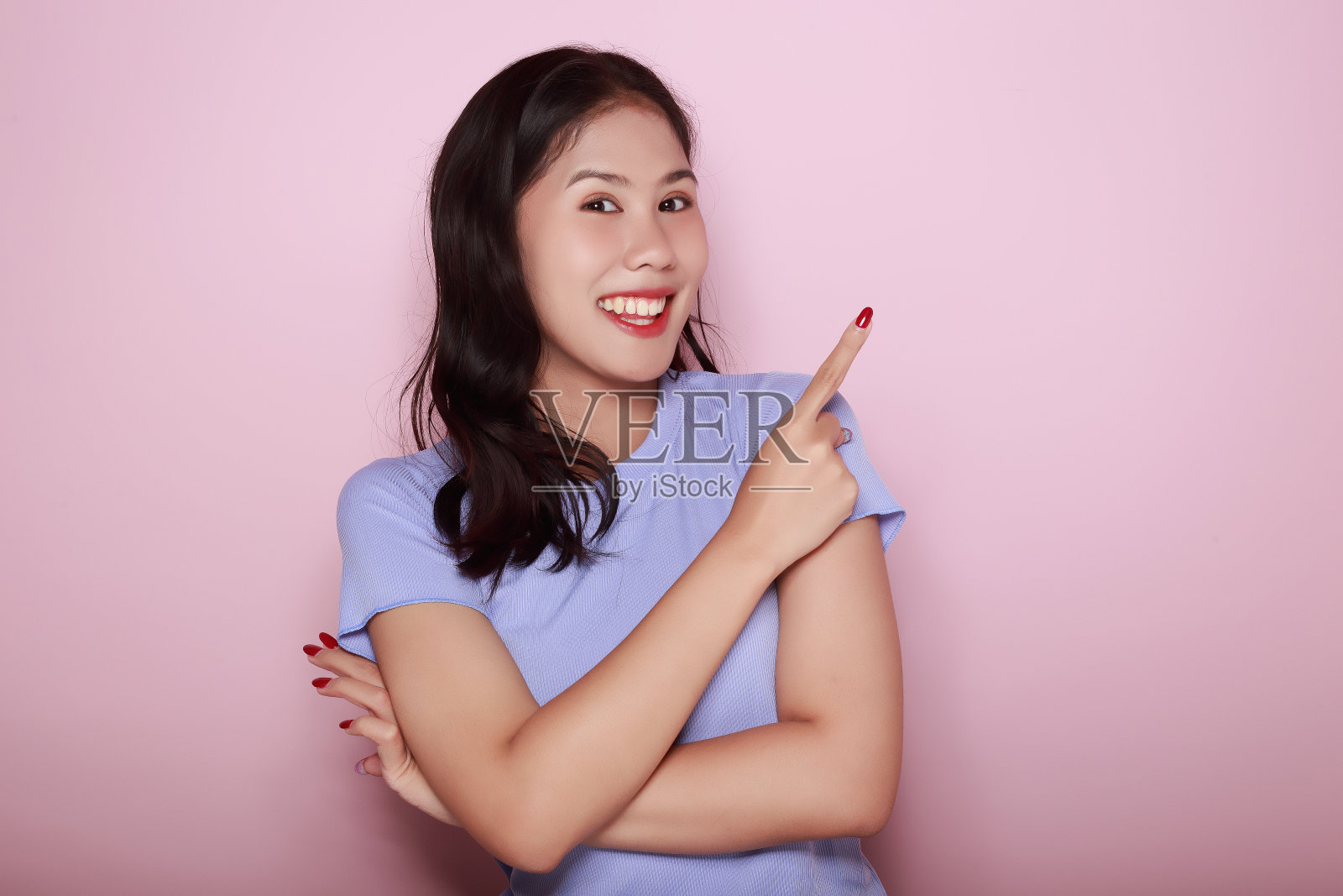 一个美丽的年轻女子的肖像，在浅粉色的背景，快乐和微笑，张贴在站立的位置，一个友好的年轻女子的肖像，快乐地微笑。照片摄影图片