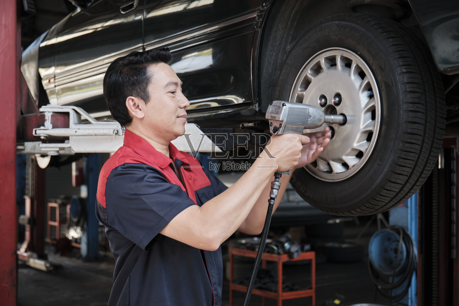 一名亚洲男性汽车技师正在服务车库换车轮。照片摄影图片