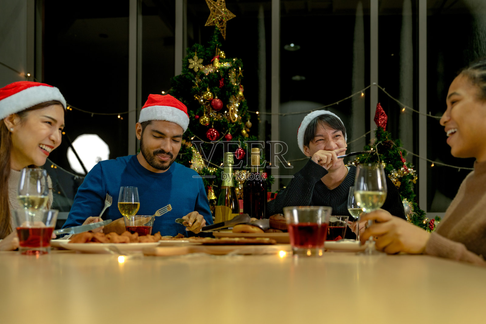 美丽的亚洲朋友男女庆祝派对。一个女人在桌子上端着披萨，还有零食和饮料。快乐朋友平安夜庆祝宴会美食和香槟酒。照片摄影图片