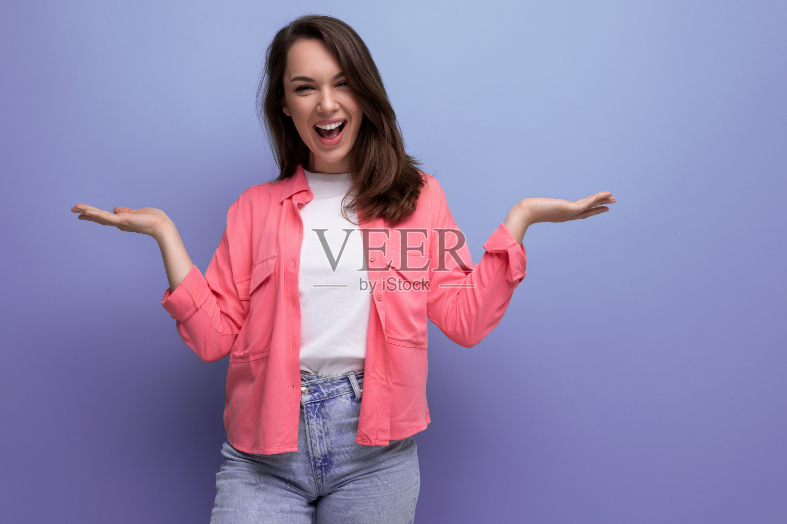 成功的欧洲年轻女性成人的肖像，齐肩的头发，粉红色的衬衫，显示喜悦的双手在工作室背景与复制空间照片摄影图片