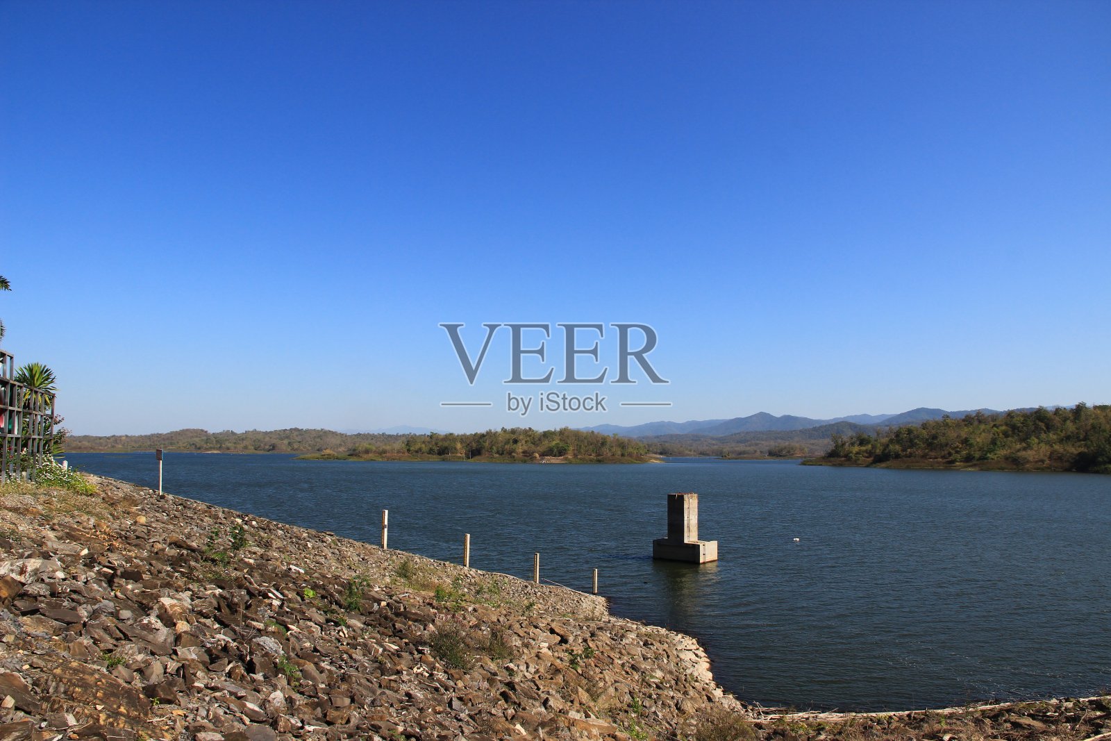 旅游景点中，有高大的树木，身后的水从大坝与蓝天为背景。照片摄影图片