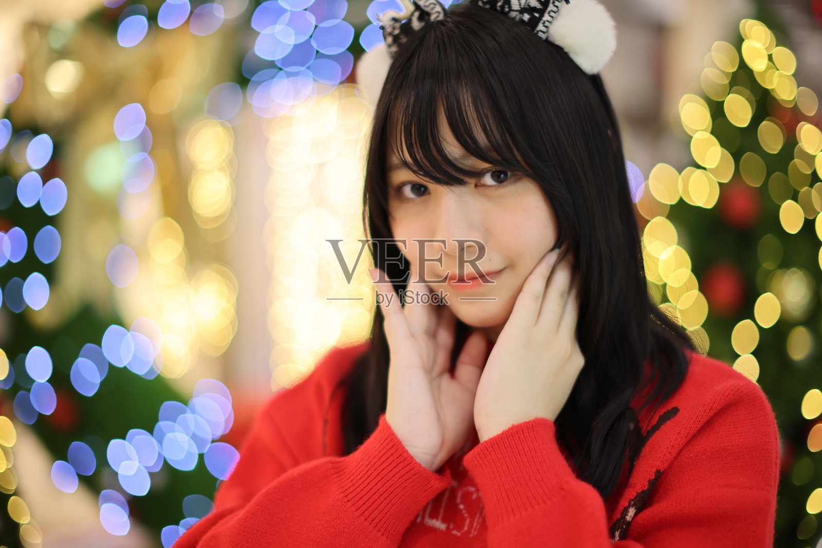 漂亮的亚洲年轻女子穿着一件红色毛衣，上面挂着圣诞树灯照片摄影图片