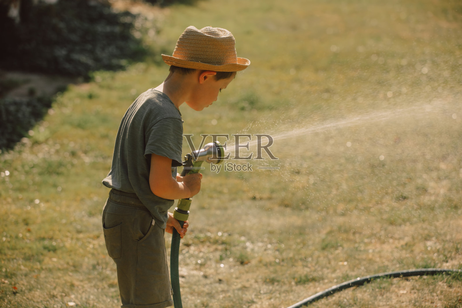 小男孩在花园里玩水管，给花和草坪浇水照片摄影图片