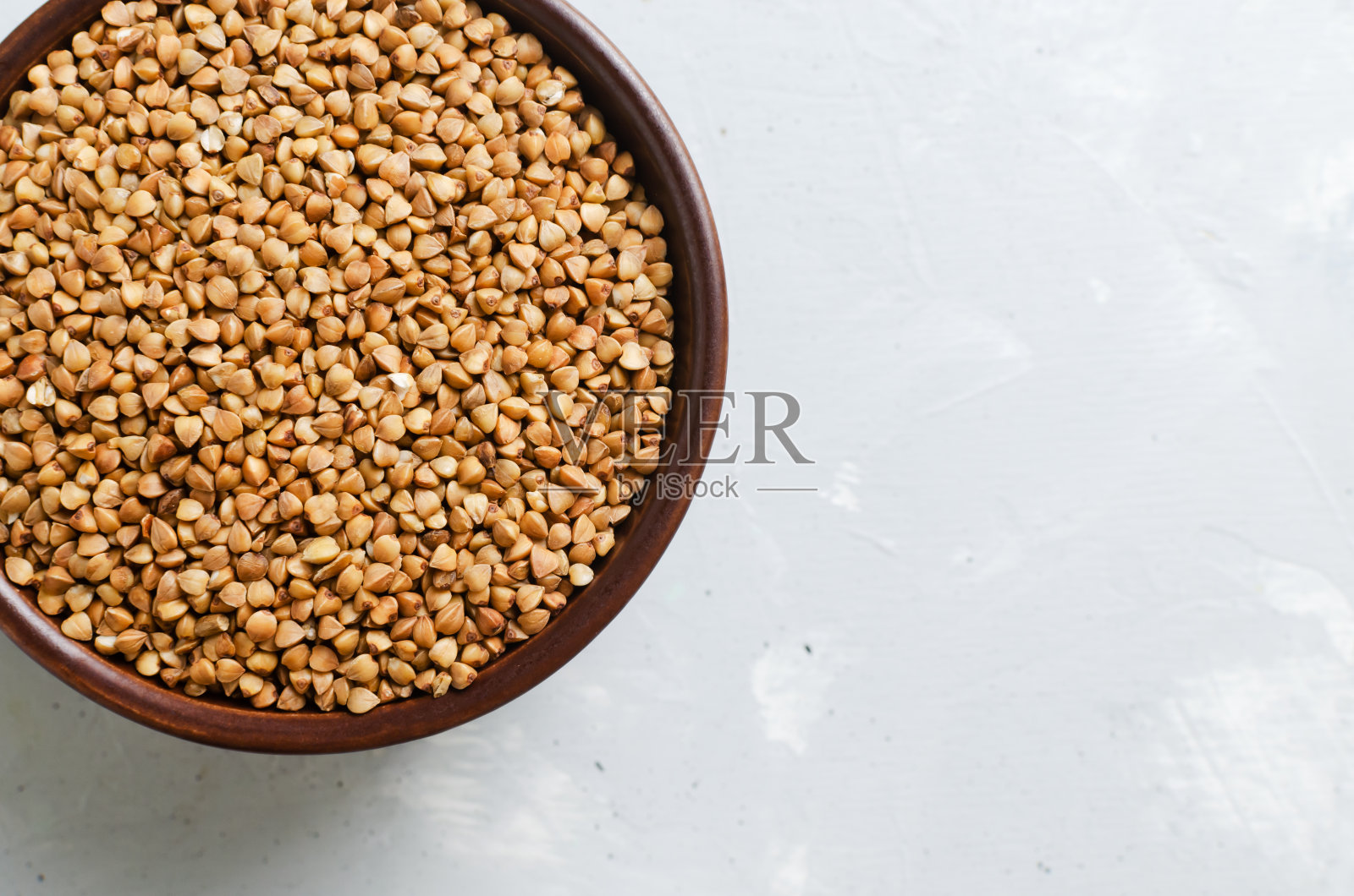 灰色背景下，棕色碗里的有机干荞麦。素食和纯素食品。健康饮食的概念。水平方向。前视图。副本的空间。照片摄影图片