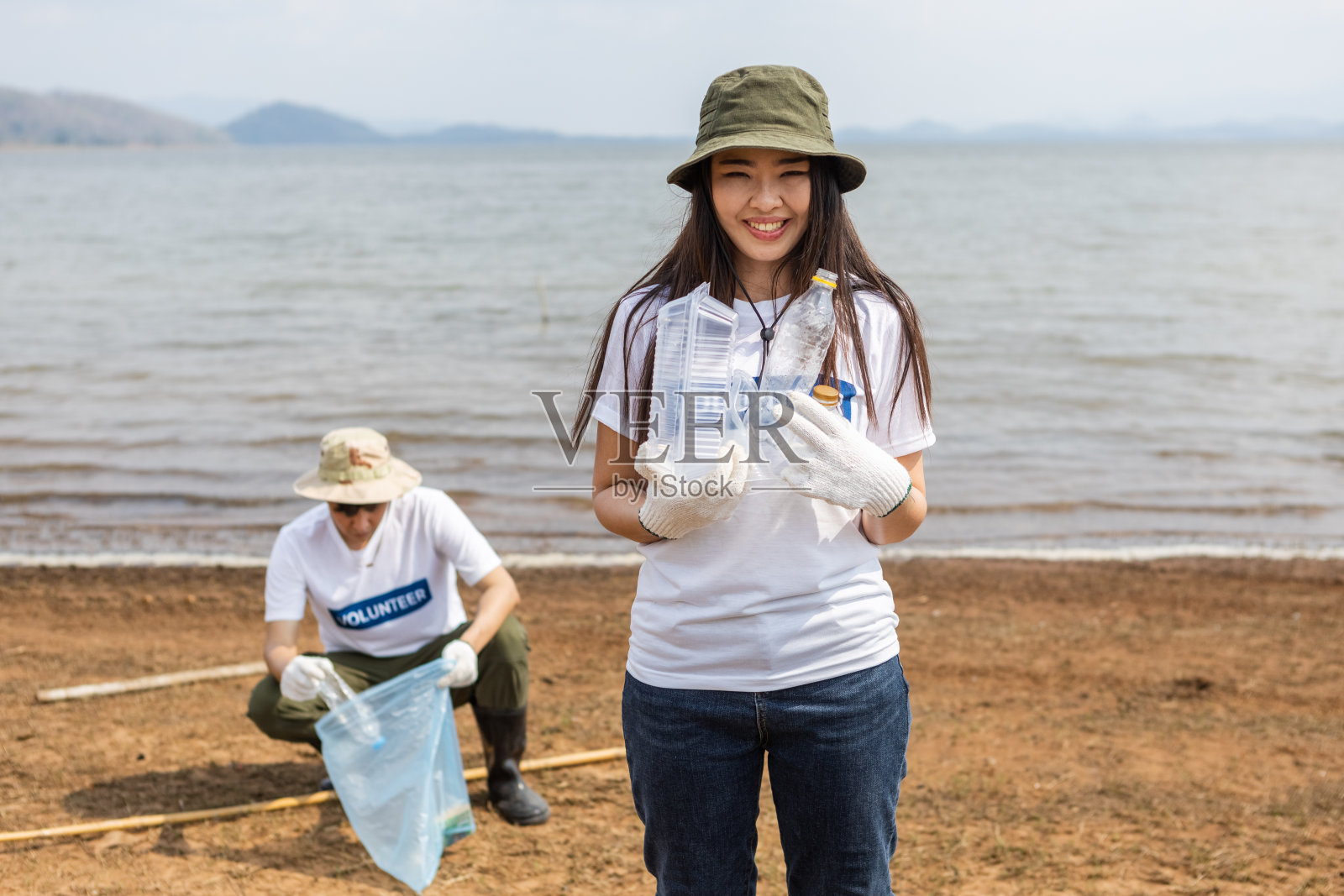 女志愿者拿着塑料瓶里的垃圾看着镜头。女性志愿者开展环境合作，拯救世界，减少全球变暖。照片摄影图片