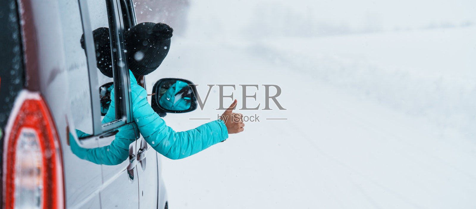 快乐的旅行者在雪地上开车，手指向上，冬季女游客从车窗欣赏雪林景色。冬季旅游，自驾游，探索和度假的概念照片摄影图片