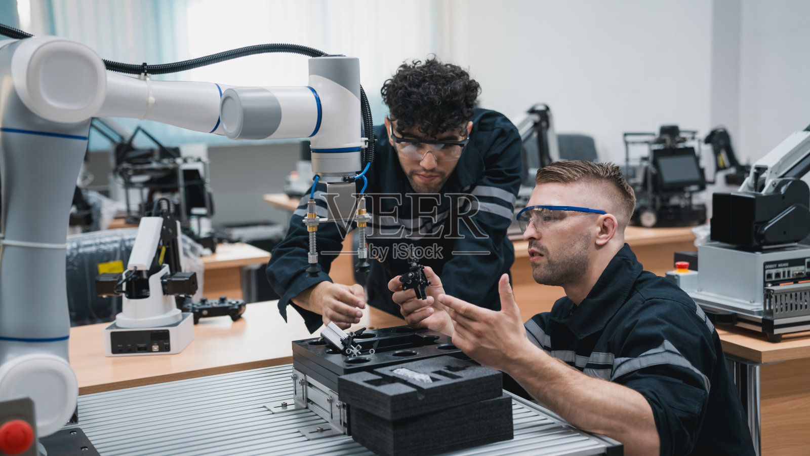 实习工程师在技术工作坊用电脑组装机械臂。服务工程师手持机器人控制器并检查机械臂焊接硬件。照片摄影图片