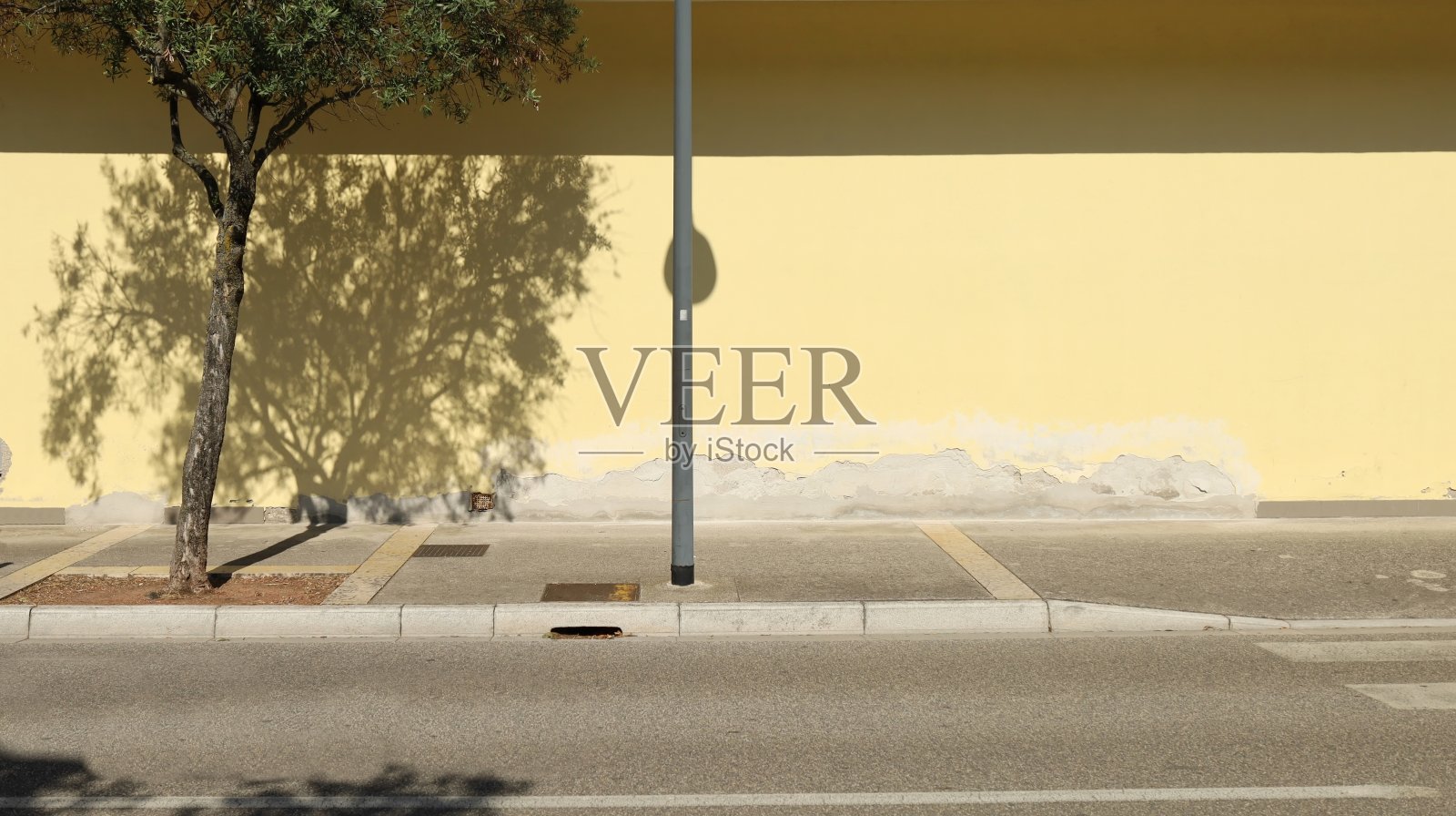 混凝土人行道上的金属杆，后面是剥落的黄色灰泥墙。街在前面，树在路边。照片摄影图片