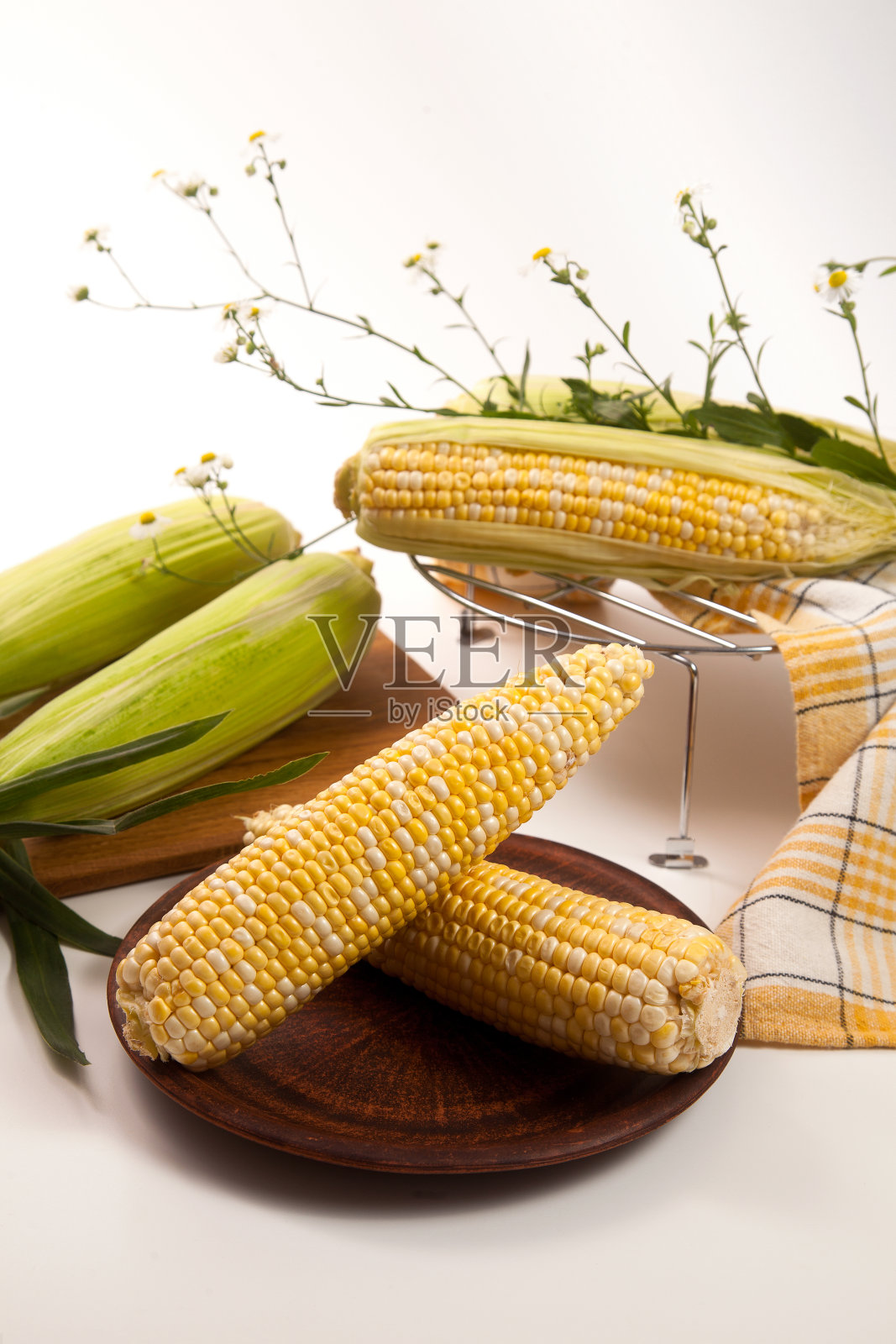白色木制背景上有几根甜玉米棒子的粘土盘子。照片摄影图片