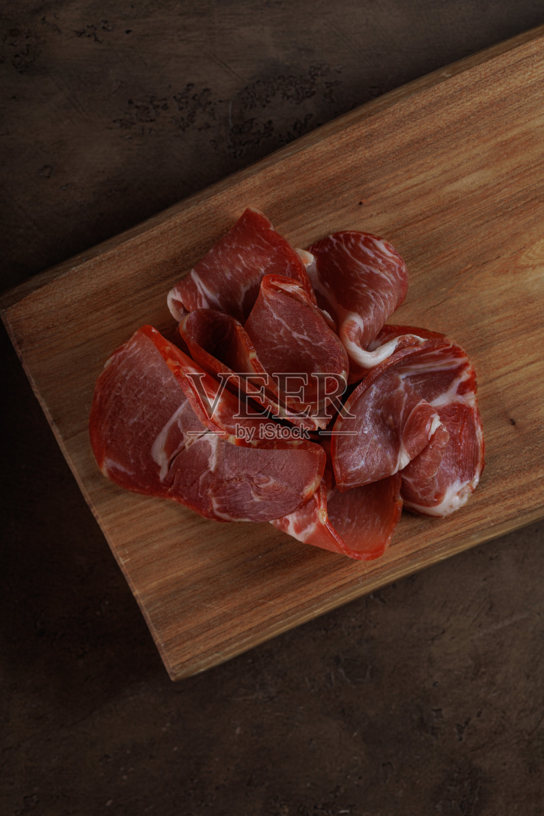 意大利熏火腿或西班牙火腿。生火腿在木制砧板上，深褐色背景。高分辨率。俯视图，复制空间照片摄影图片