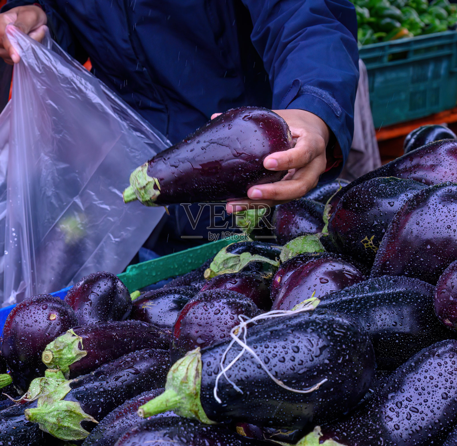 一名妇女冒雨在市场里把茄子装进塑料袋里。照片摄影图片