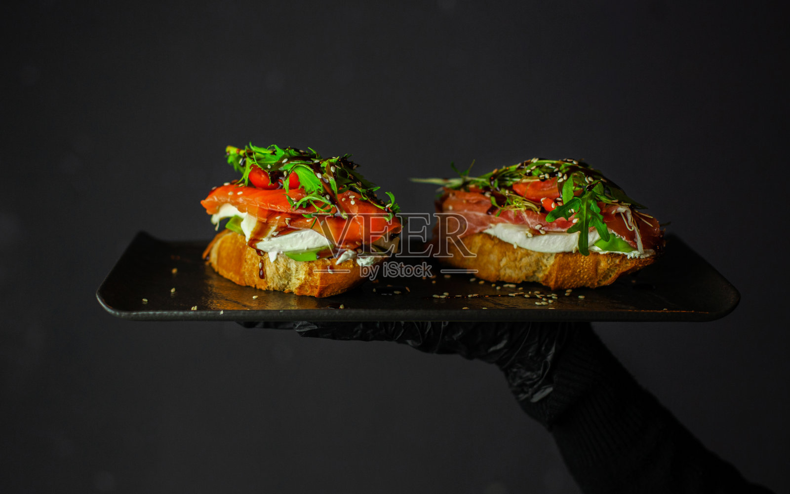 厨师手里拿着黑色盘子里的火腿、火腿、新鲜吐司片。意式烤面包照片摄影图片