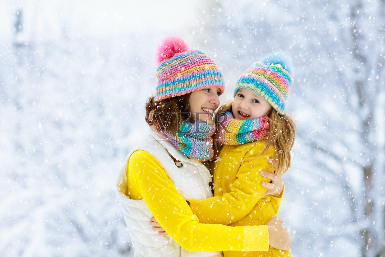 雪中，母亲和孩子戴着编织的冬帽。照片摄影图片