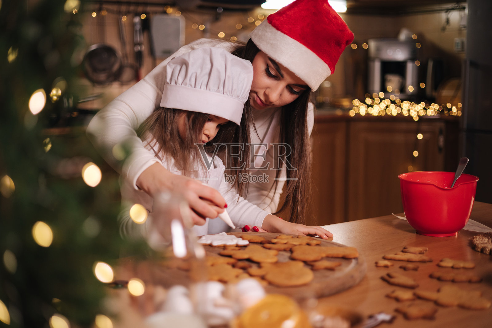 快乐的小女孩和她美丽的妈妈在家里做姜饼。厨房的圣诞装饰。有仙女灯的冷杉树照片摄影图片