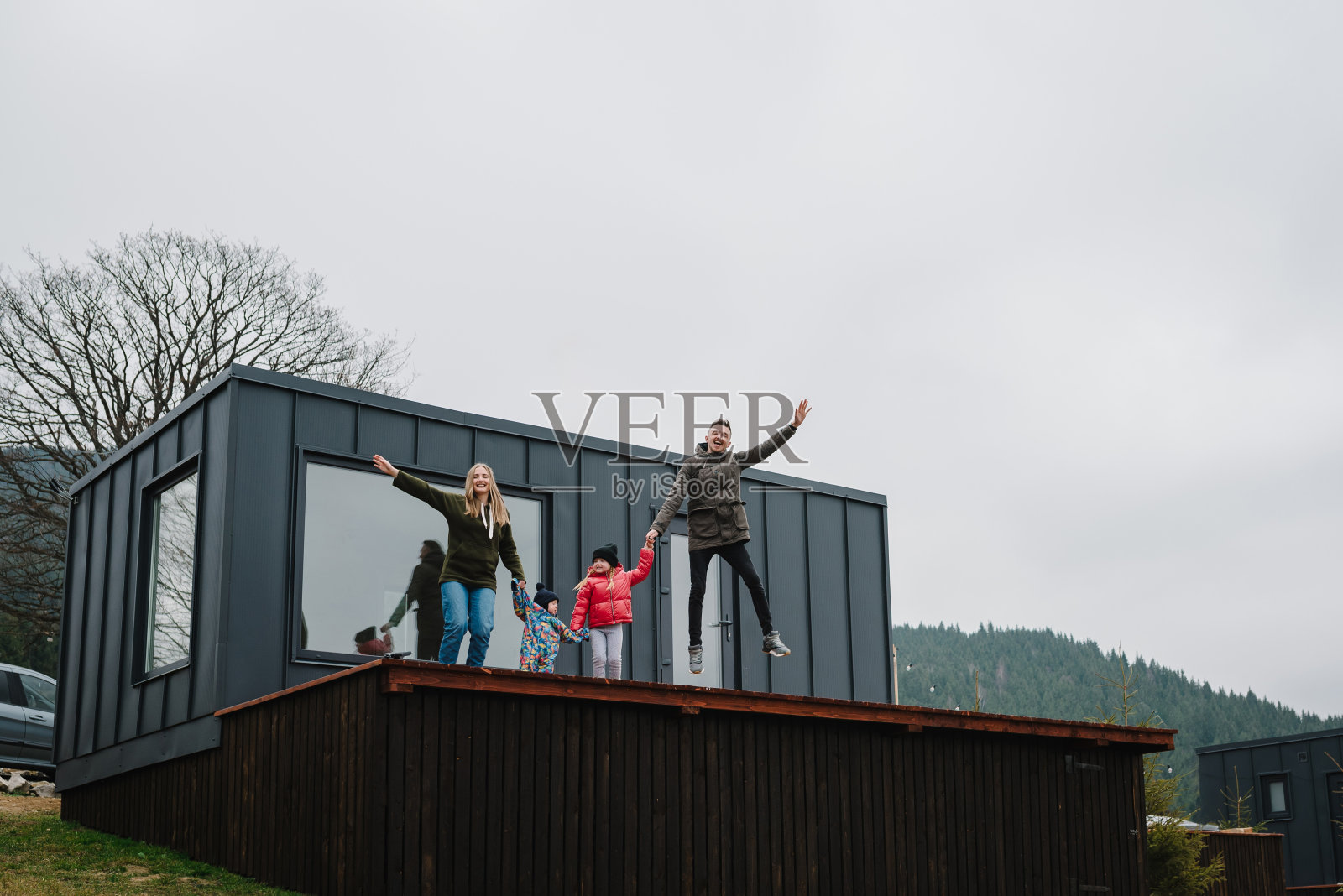 人们站在乡间别墅的后院。秋天的一天，母亲、父亲在露台上牵着孩子们的手。妈妈，爸爸拥抱女儿，儿子一起享受时光。带着孩子去山里度假。照片摄影图片