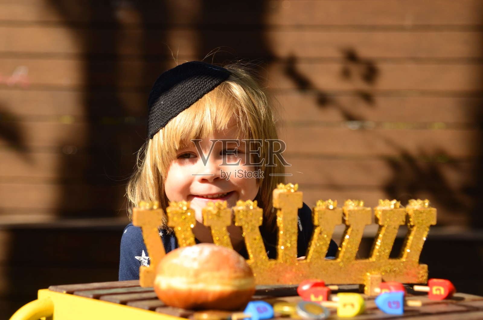 戴着小圆帽的可爱男孩庆祝光明节，想吃油炸圈饼。孩子笑了照片摄影图片