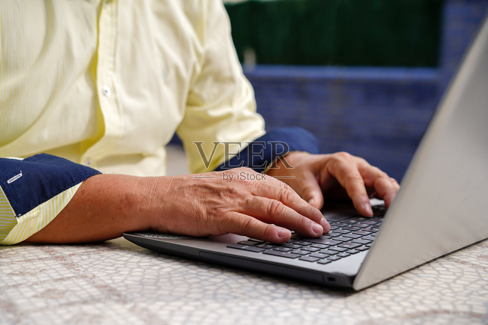 一个无法辨认的数字游牧民的特写镜头，他穿着西装，在外面的笔记本电脑键盘上打字。照片摄影图片