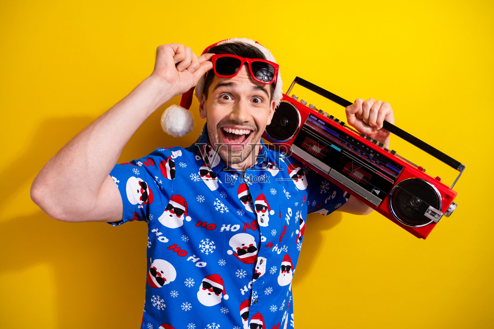 照片中，惊喜的家伙拿着音箱，手臂触摸着太阳眼镜，在黄色背景上孤立的节日活动照片摄影图片