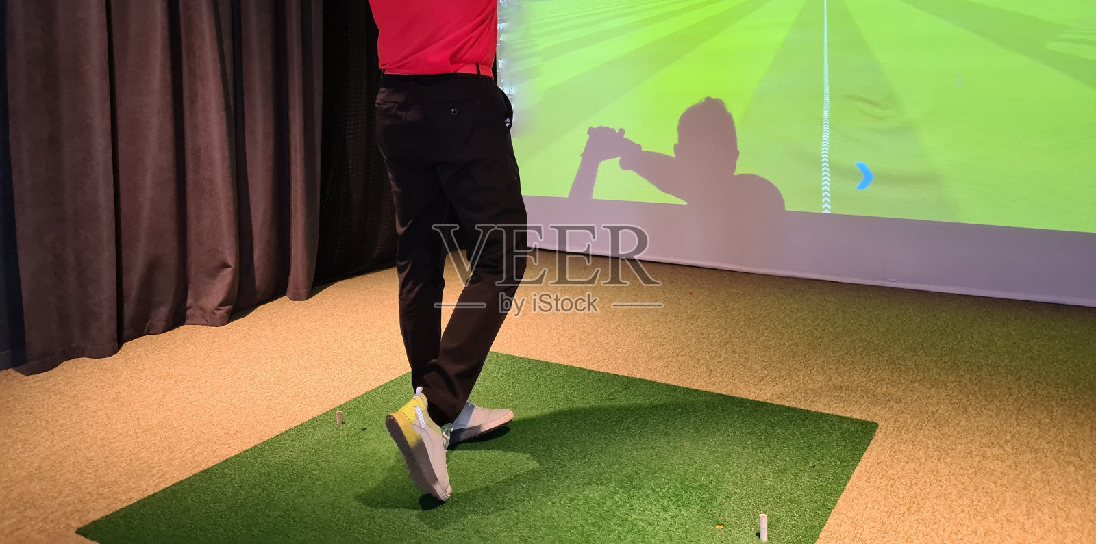 年轻人在室内打高尔夫球。高尔夫模拟器照片摄影图片