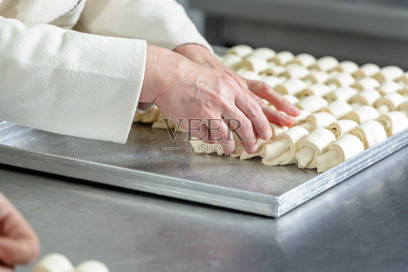 在小生意的厨房柜台上，面包师的手在烤盘里排列着新月形的面包卷照片摄影图片