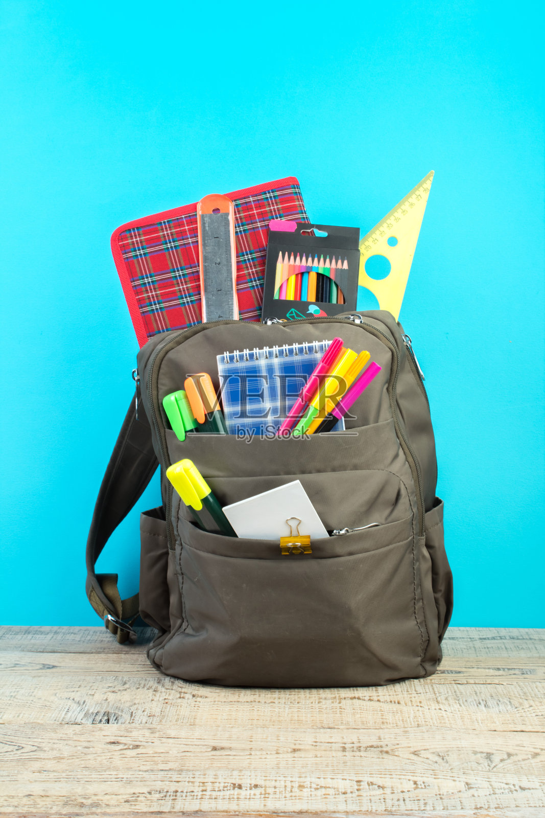 背包里有不同颜色的文具放在桌子上。蓝色背景。回到学校。照片摄影图片