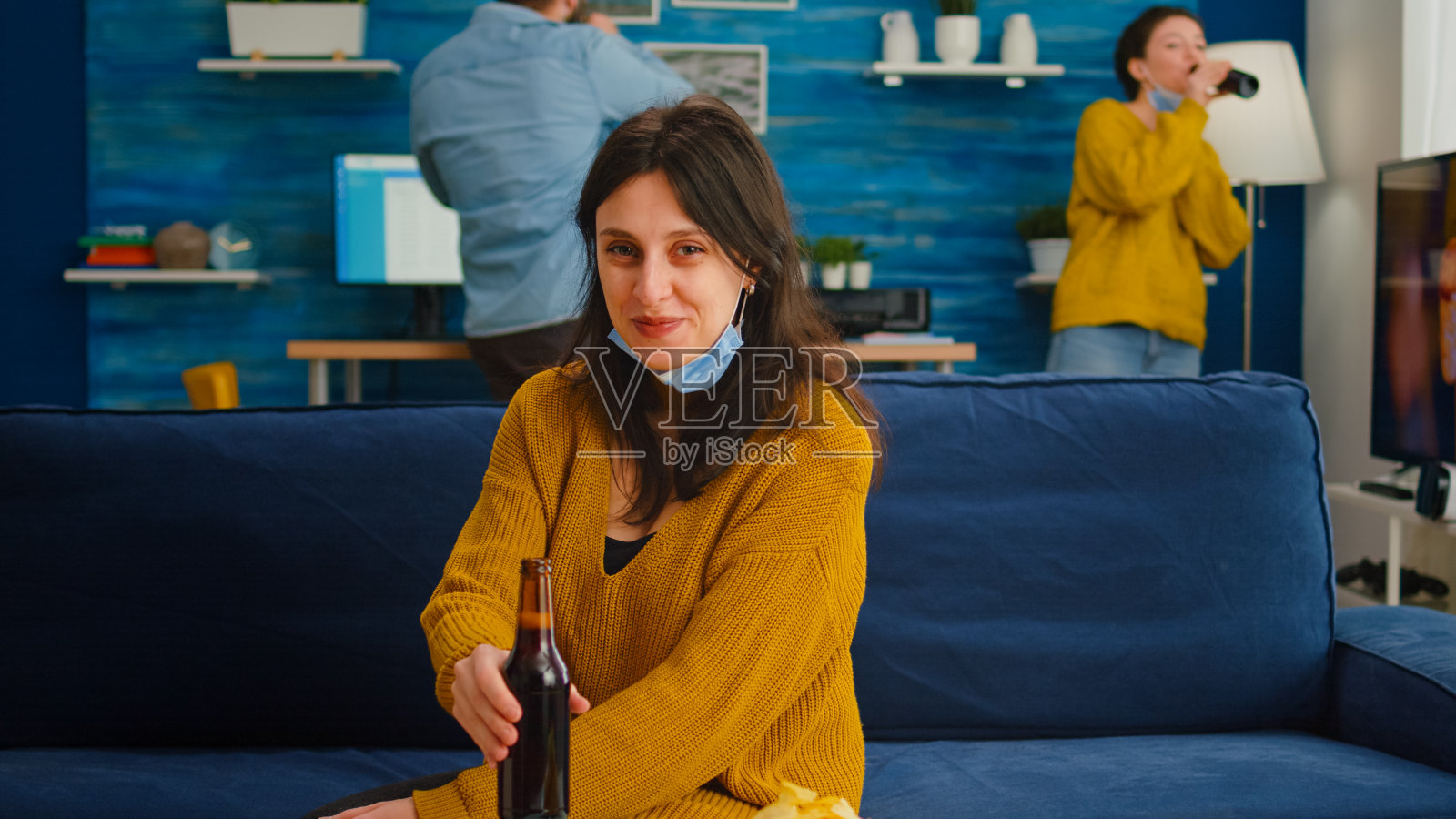 戴着防护面具的年轻女士在客厅喝啤酒照片摄影图片