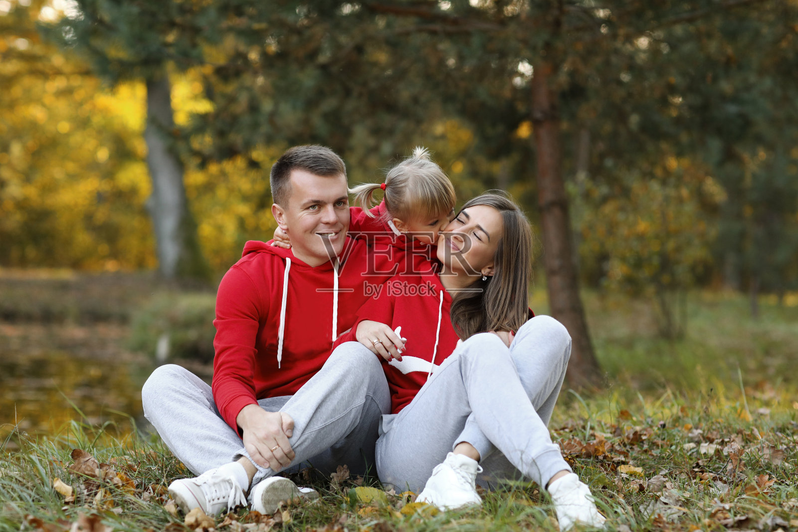 小女儿在秋天的公园里亲吻和拥抱爸爸妈妈。家庭度假的概念。父亲节，母亲节，婴儿节。共度时光。家人看。照片摄影图片