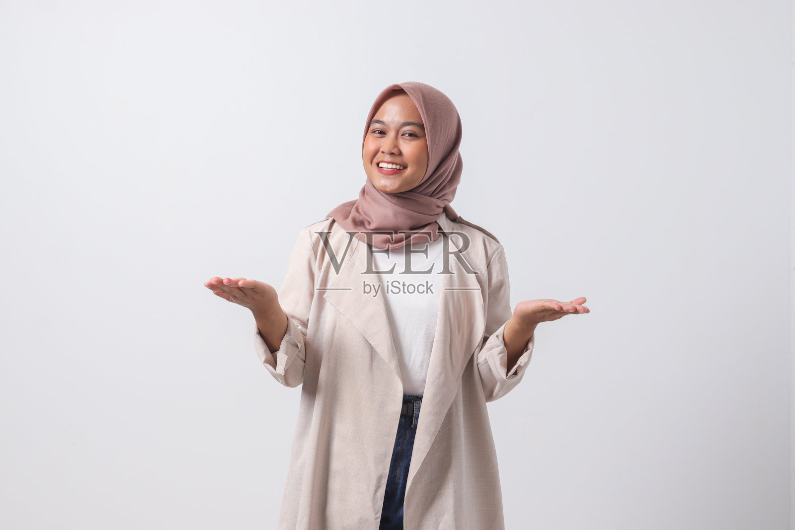一名穿着休闲西装、戴着头巾的亚洲女性的肖像，她的双手向两侧摊开。问候和欢迎某人。邀请人们进来。商人的概念。白色背景上的孤立图像照片摄影图片