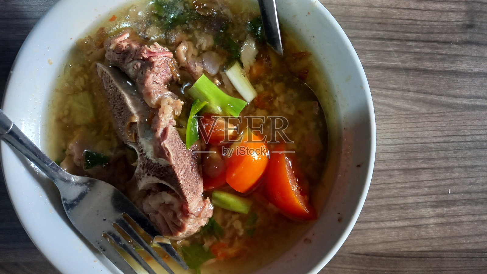 牛肉排骨汤，用葱和番茄切片混合，在一个白色的碗里照片摄影图片