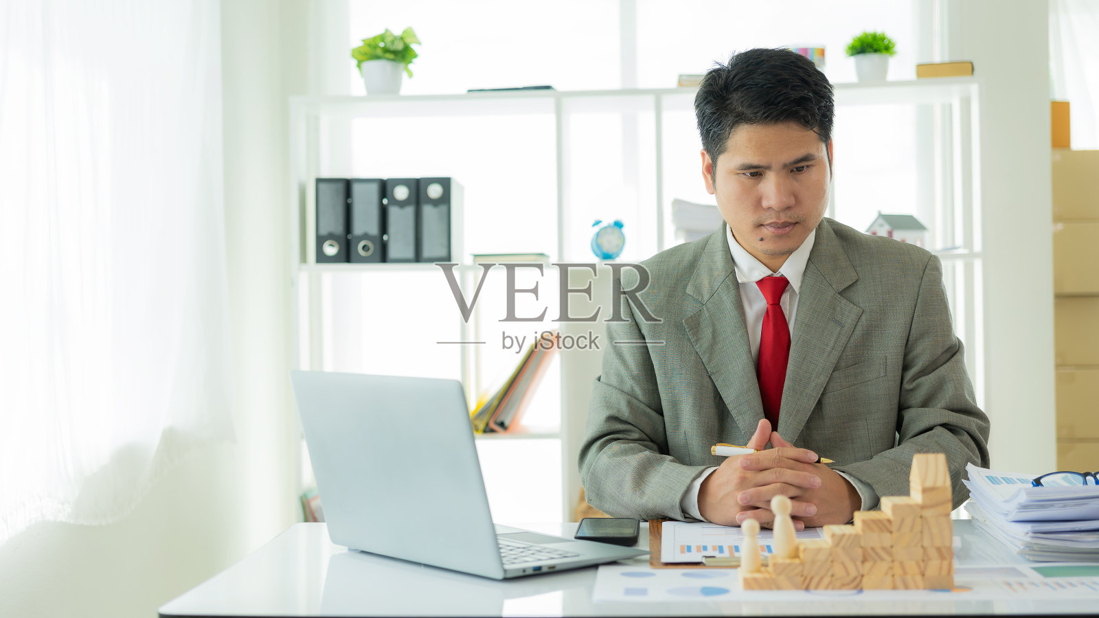 年轻的亚洲商人查看公司预算报表。分配应收账款生产控制业务风险概念，前面有木块照片摄影图片