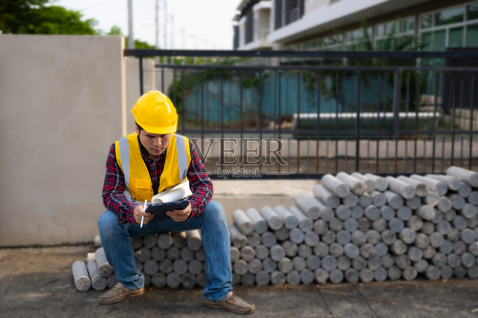 戴着头盔的年轻的亚洲土木工程师或建筑监理在检查施工现场时，目光转向别处，露出微笑。照片摄影图片