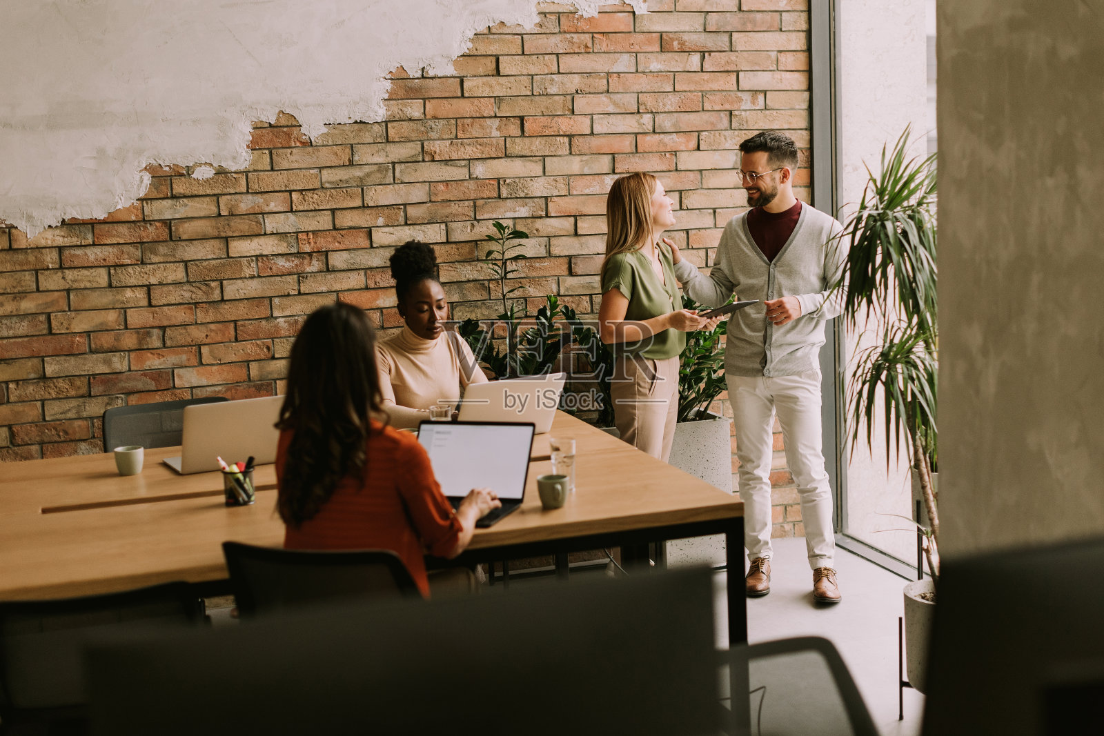 年轻的多民族创业团队在工业风格办公室的砖墙旁工作照片摄影图片