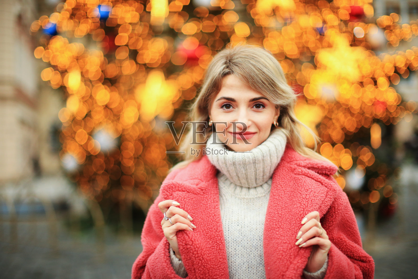 一个穿着粉色皮大衣的女孩站在圣诞树的背景下，手里拿着一个烟花照片摄影图片