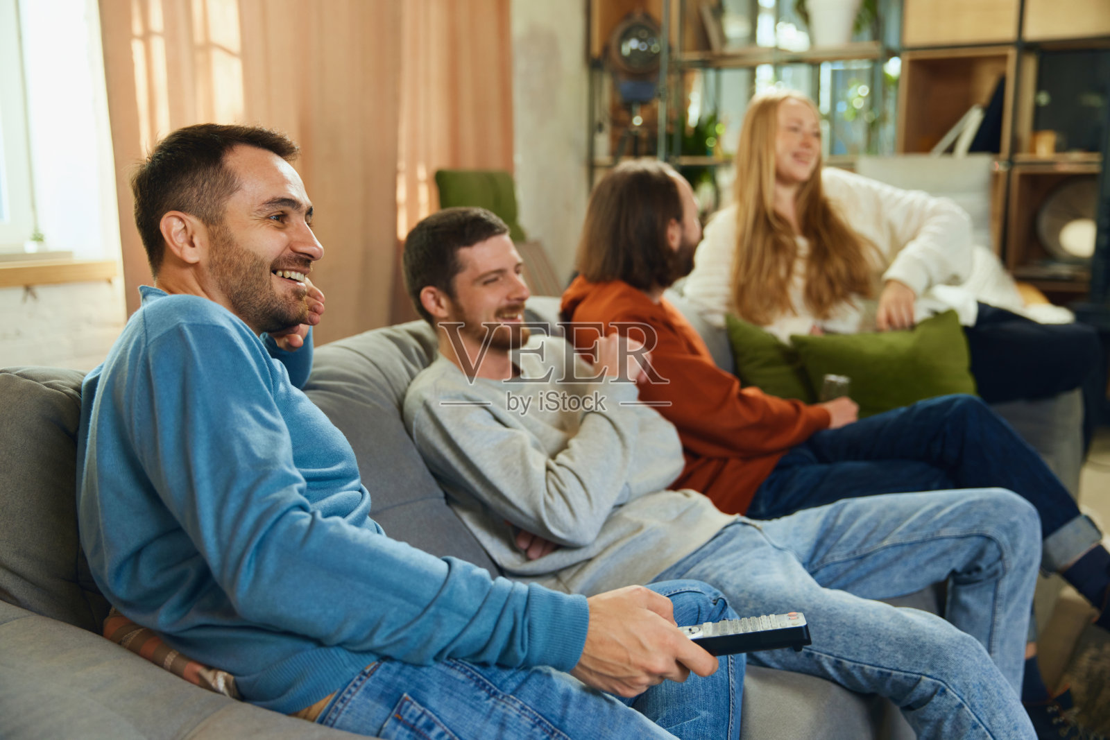 快乐的人们坐在客厅的沙发上，一边看喜剧电影、电视节目一边讨论。有选择性的重点。照片摄影图片