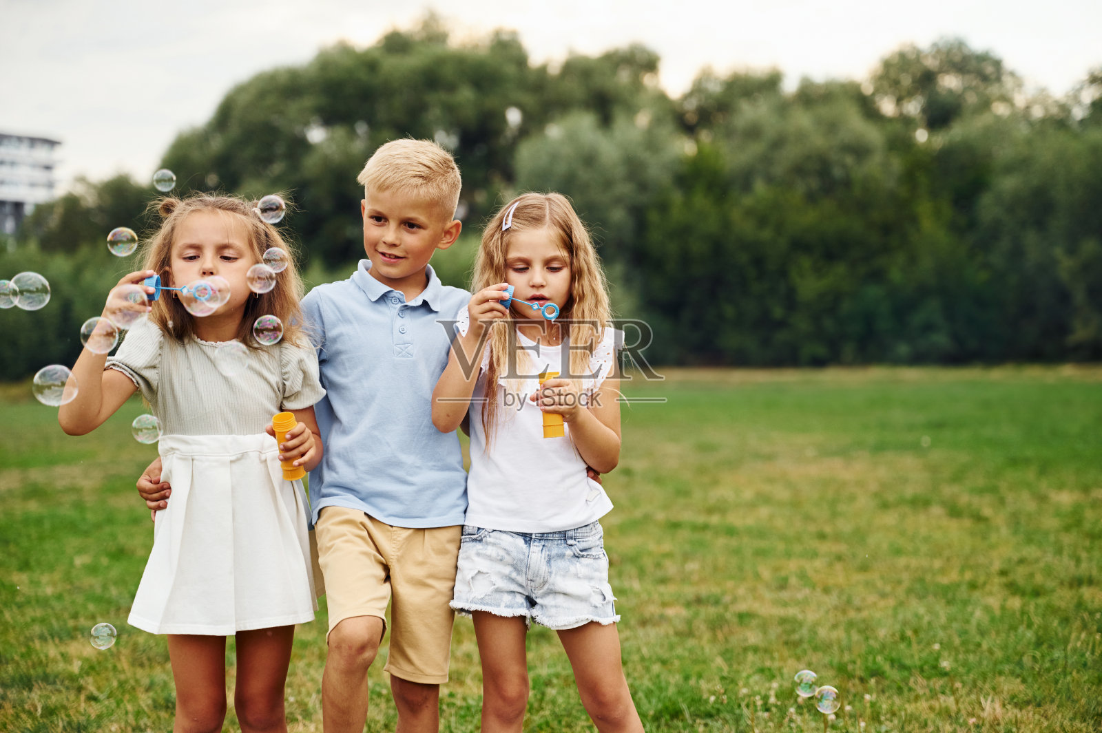 男孩和两个女孩在玩泡泡。孩子们白天一起在操场上玩得很开心照片摄影图片