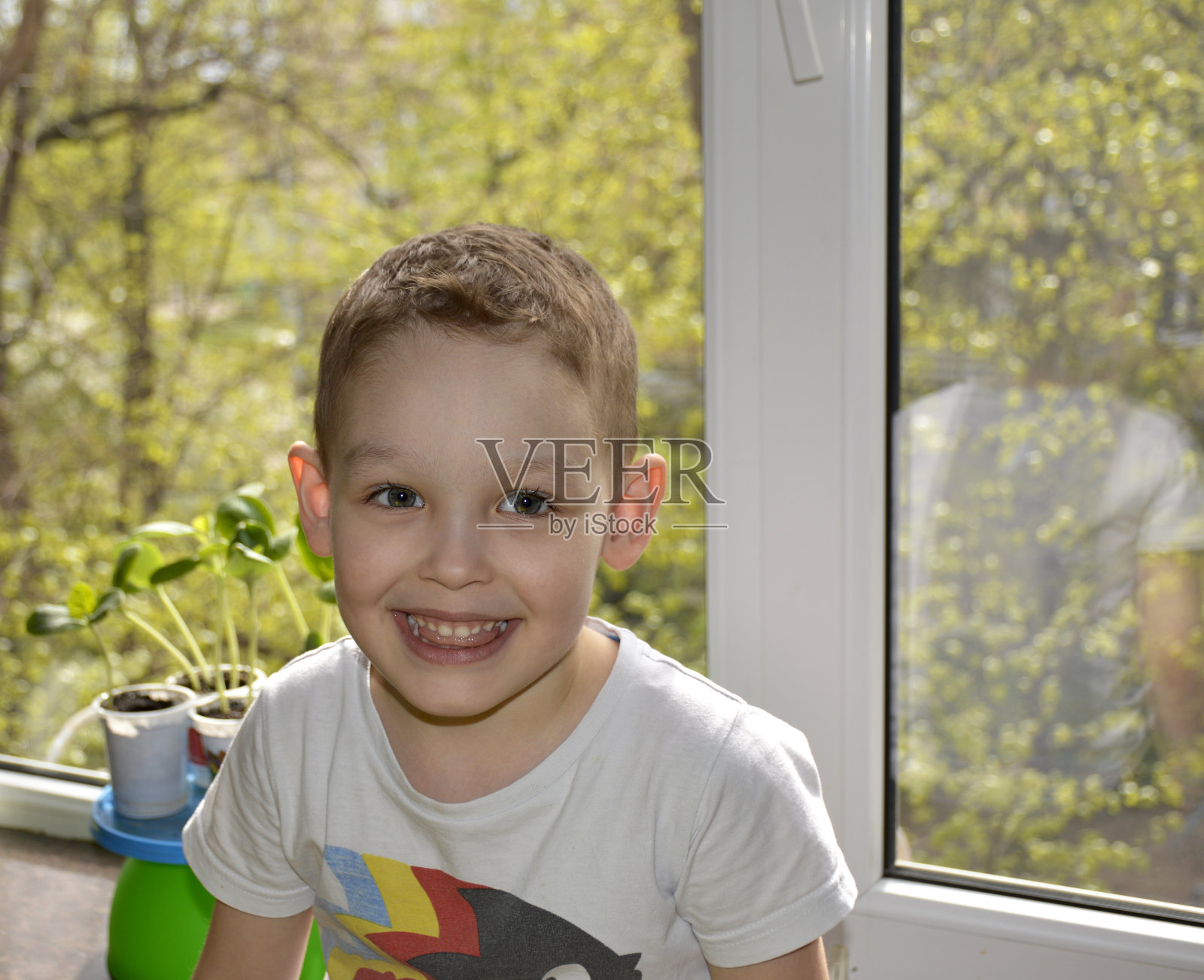 一个小男孩坐在窗边，看着相机，开心地笑着照片摄影图片