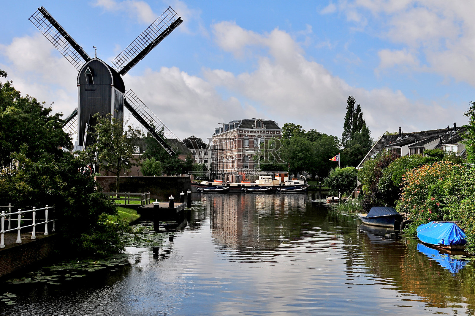 船只停泊在荷兰莱顿的运河上，远处是风车照片摄影图片